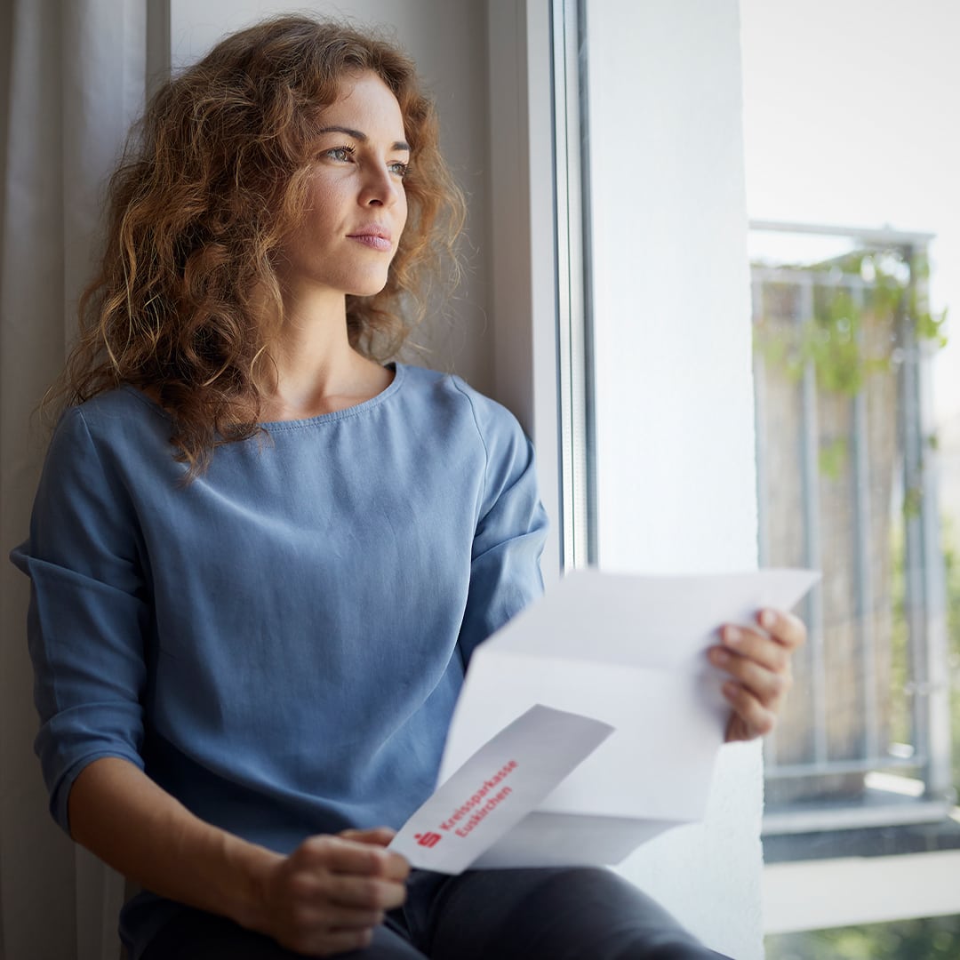 Eine Frau sitzt auf einer Fensterbank und hält einen geöffneten Brief in der Hand
