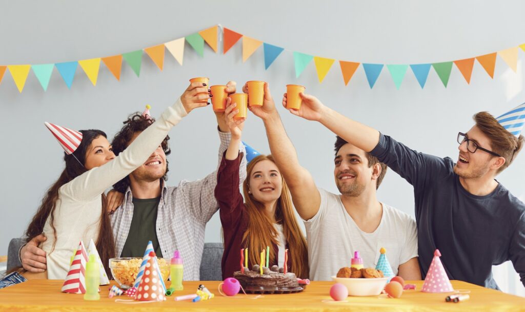 Eine Gruppe junger Menschen mit Partyhut sitzen vor einem Tisch, der mit Kuchen gedeckt ist