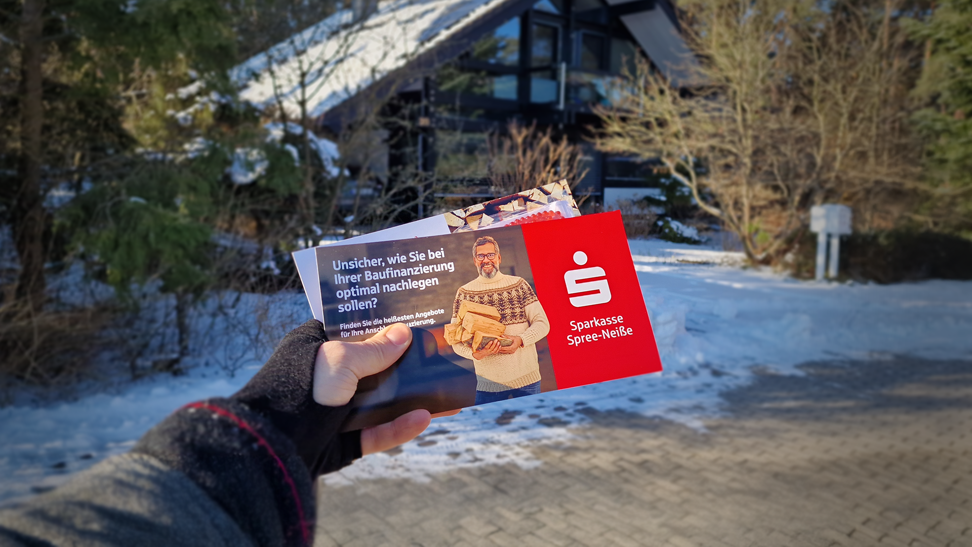 Der Promoter hebt die Postkarte in die Luft, die gerade verteilt wurde. Im Hintergrund erblickt man das Gebäude, in dessen Briefkasten die Postkarte bald ihren Platz finden wird.