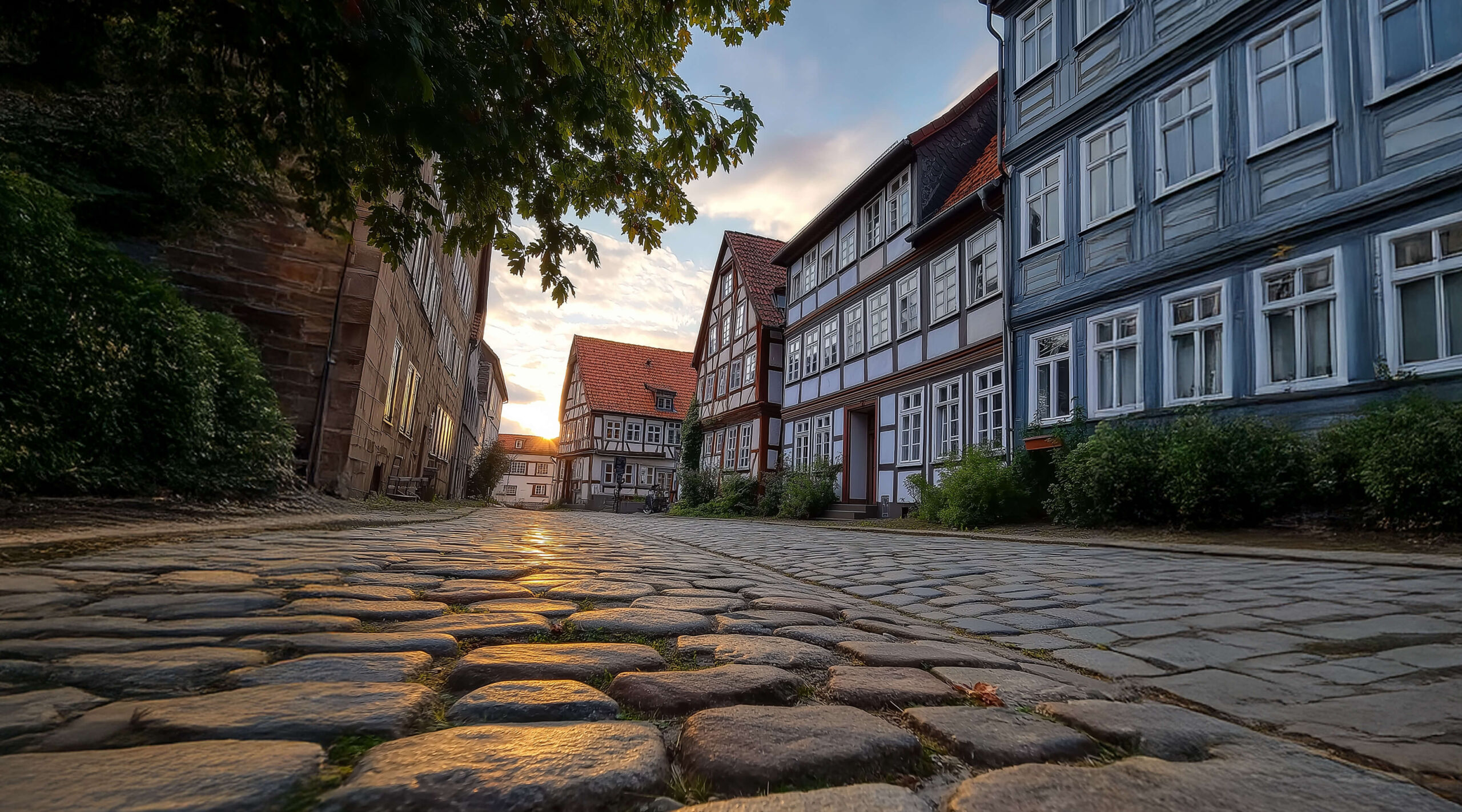 Straße mit Kopfsteinpflaster gesäumt von Fachwerkhäusern. Die Sonne geht unter und taucht die Straße in ein warmes Licht.