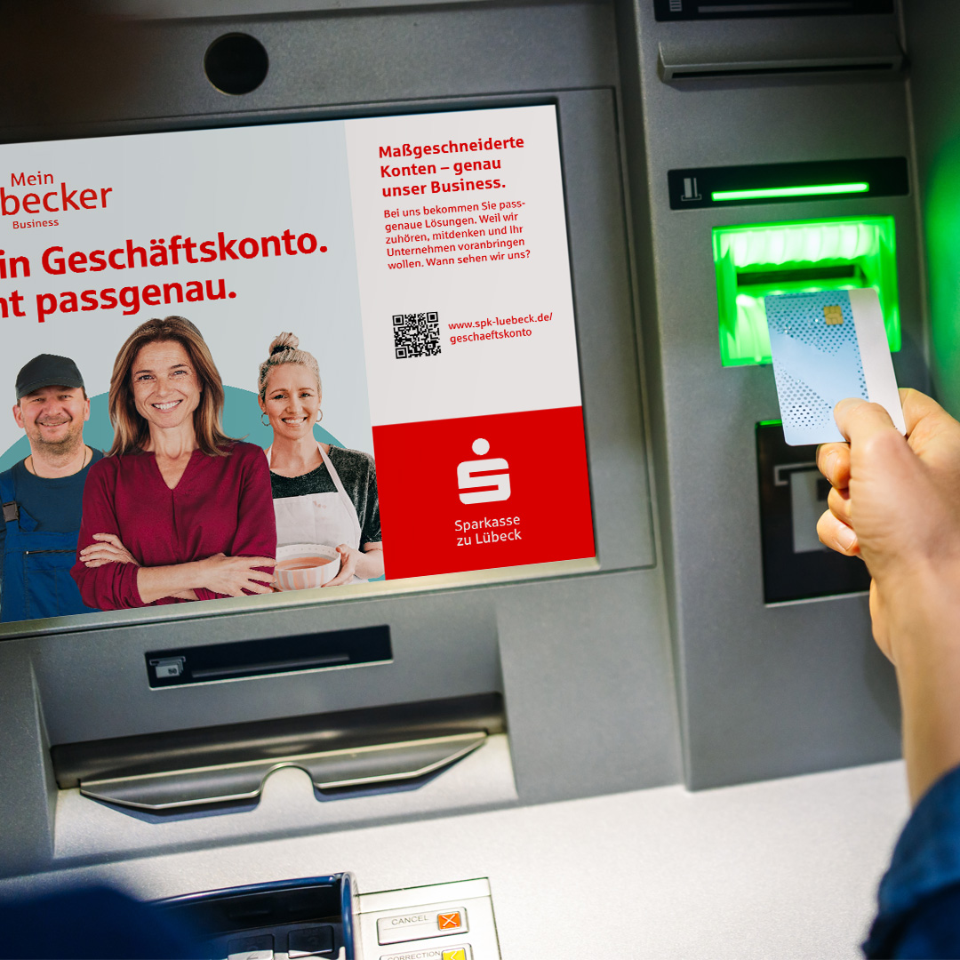 Werbeansicht auf einem Geldautomaten zeigt 3 Geschäfts-Personen. Sie stehen wir das Mein Lübecker Businesskonto